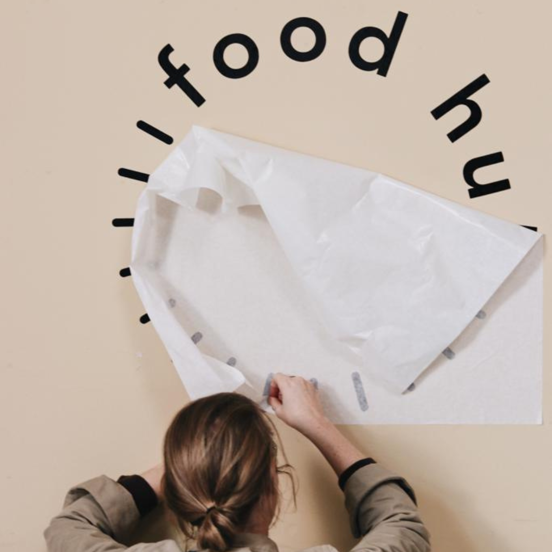 Photo of person putting a sticker with the Food Hub logo on a wall